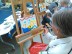 Eine Frau sitzt an einer Staffelei und malt ein Bild.