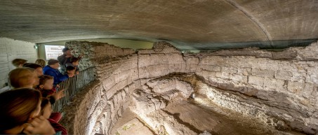 Menschen schauen sich eine unterirdische Ausgrabung mit alten Mauern aus der Römerzeit an.