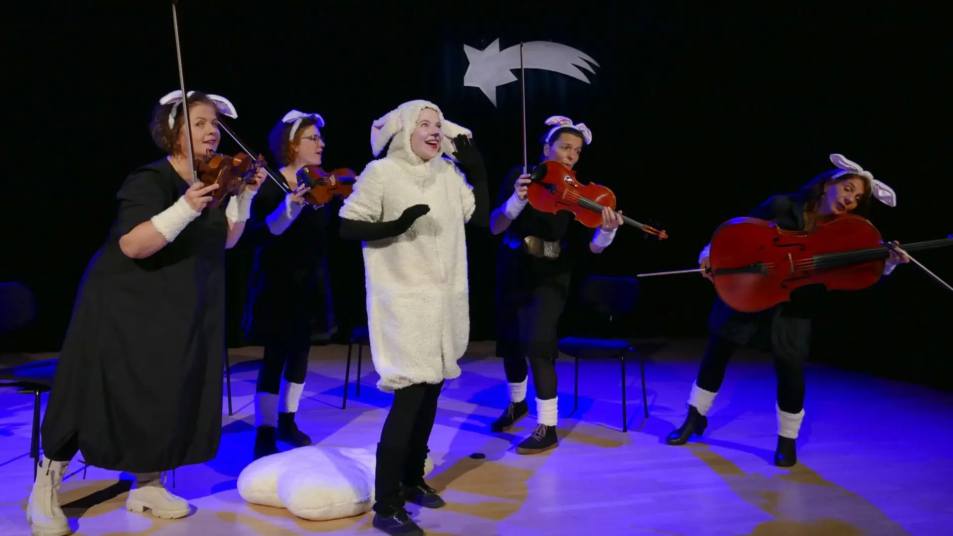 Foto von Schauspieler in Schafskostüm und Musiker*innen