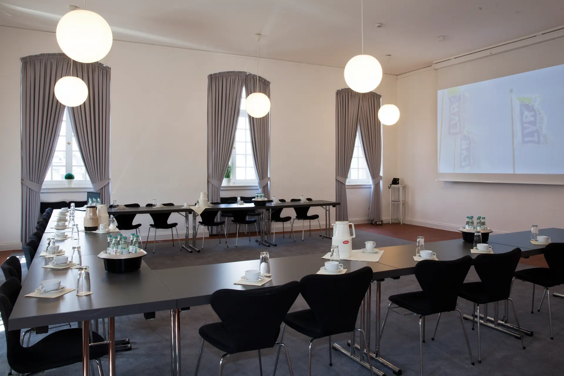 Foto von Tischen im Mathildensaal mit Beamer und Leinwand