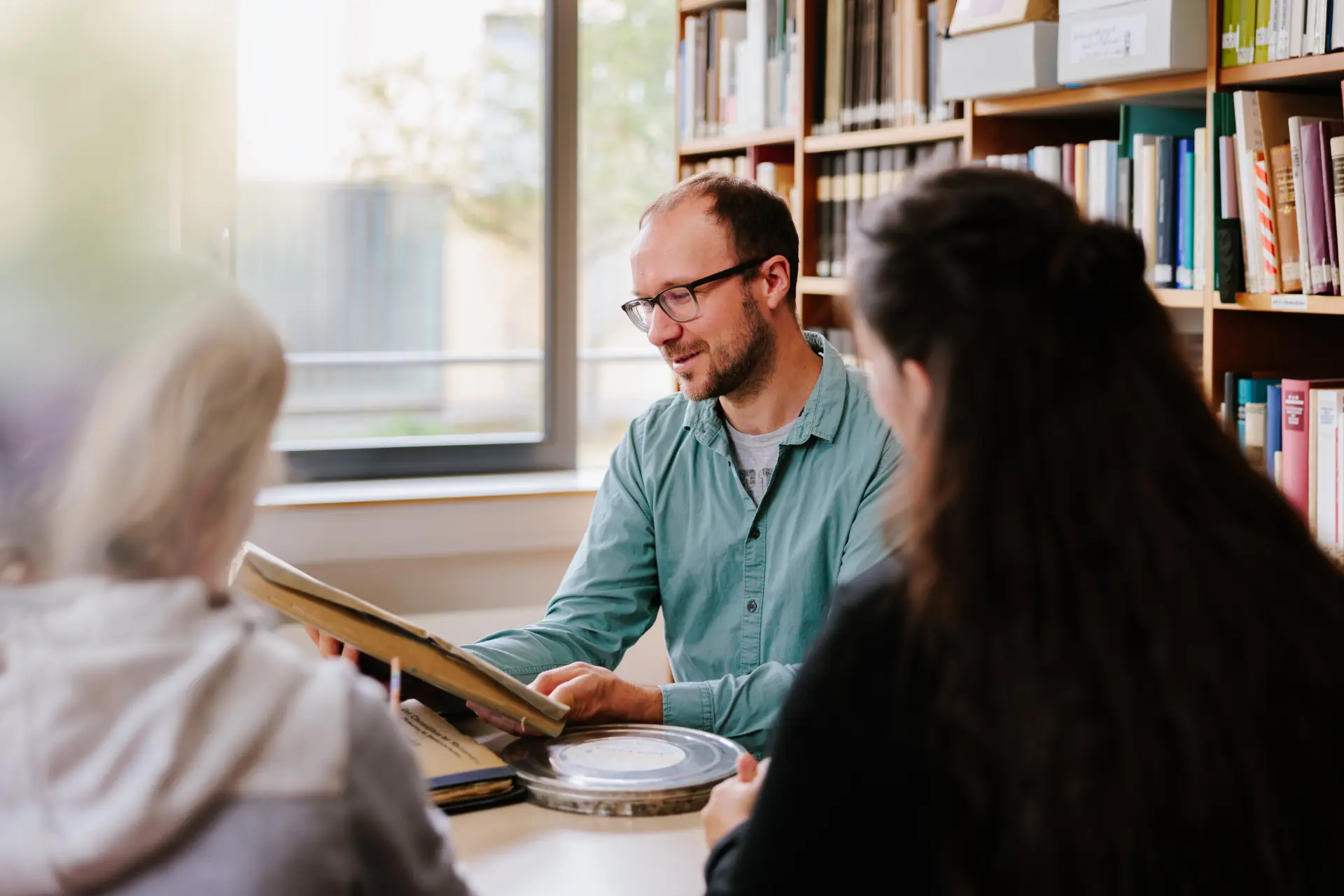 Foto von drei Personen an einem Tisch, im Gespräch, eine betrachtet eine alte Akte.