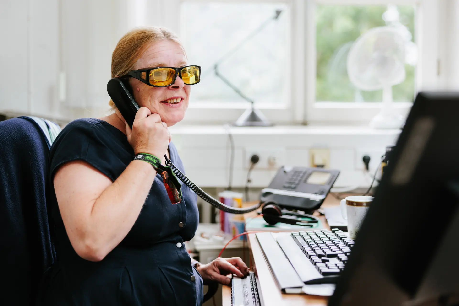 Foto einer Frau am Schreibtisch, die einen Telefonhörer am Ohr hält.