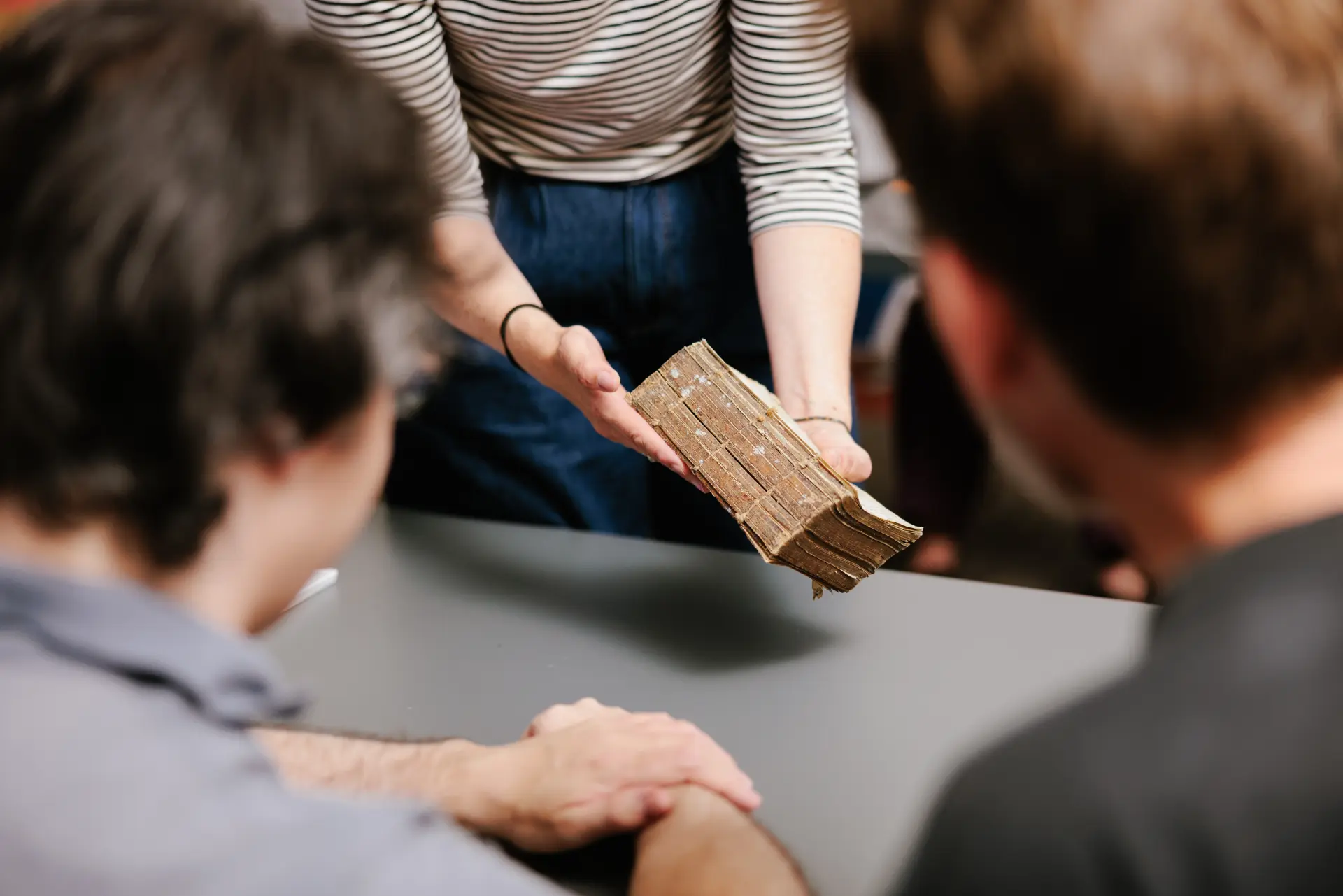 Foto einer Person, die ein altes Buch in den Händen hält und es zwei anderen Personen zeigt.