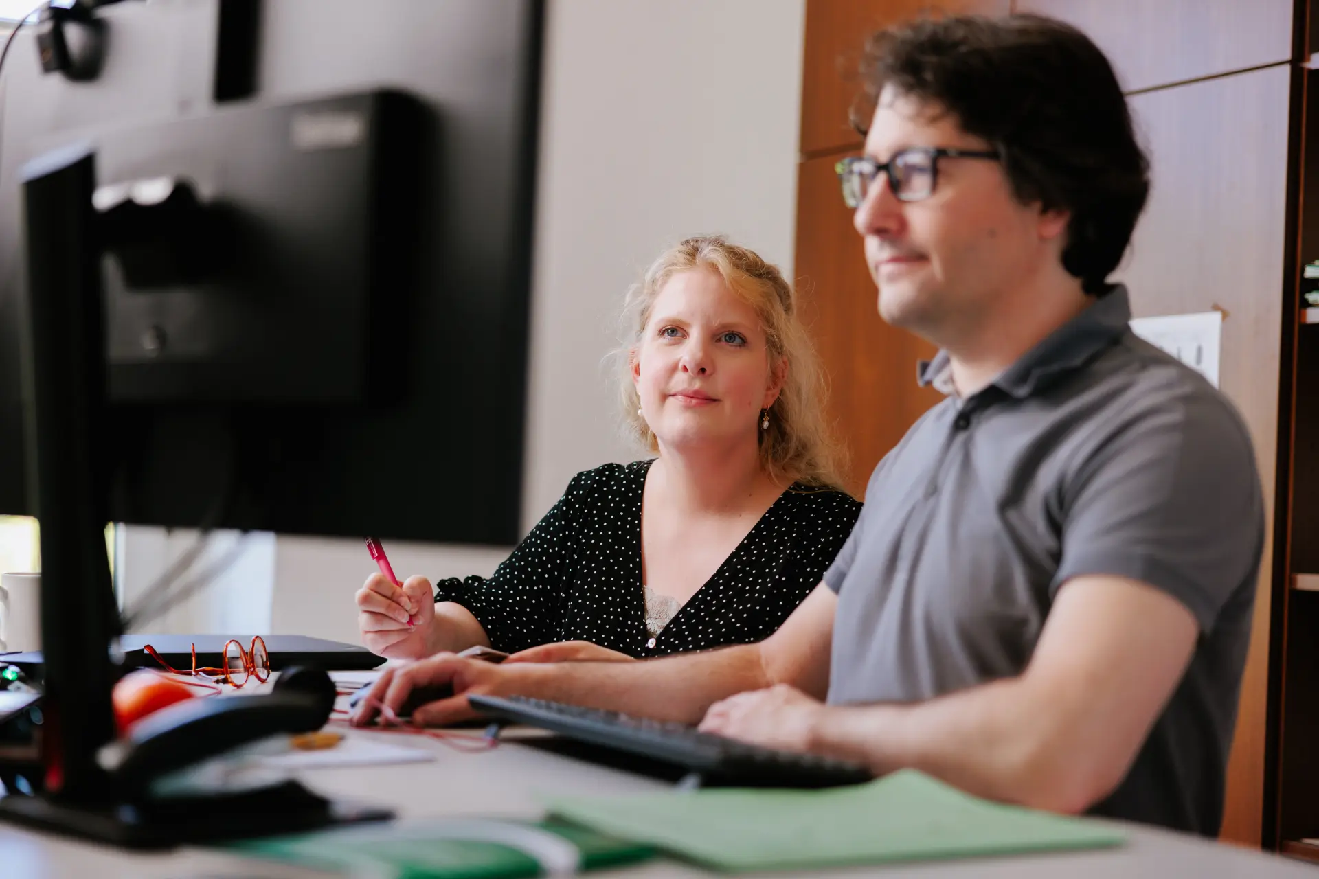 Foto von zwei Personen hinter einem Schreibtisch, die auf einen Computerbildschirm blicken.