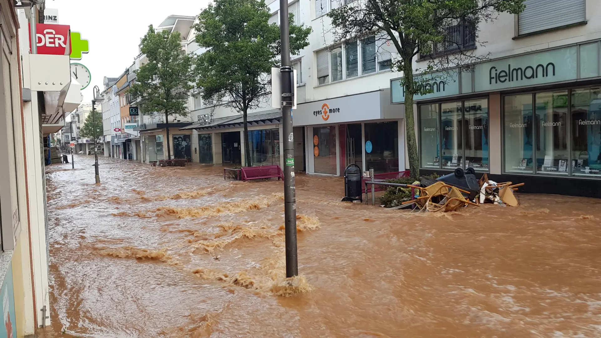 Foto eines Stroms aus braunem Wasser das durch die Innenstadt von Euskirchen vorbei an Häusern und Geschäften fließt.