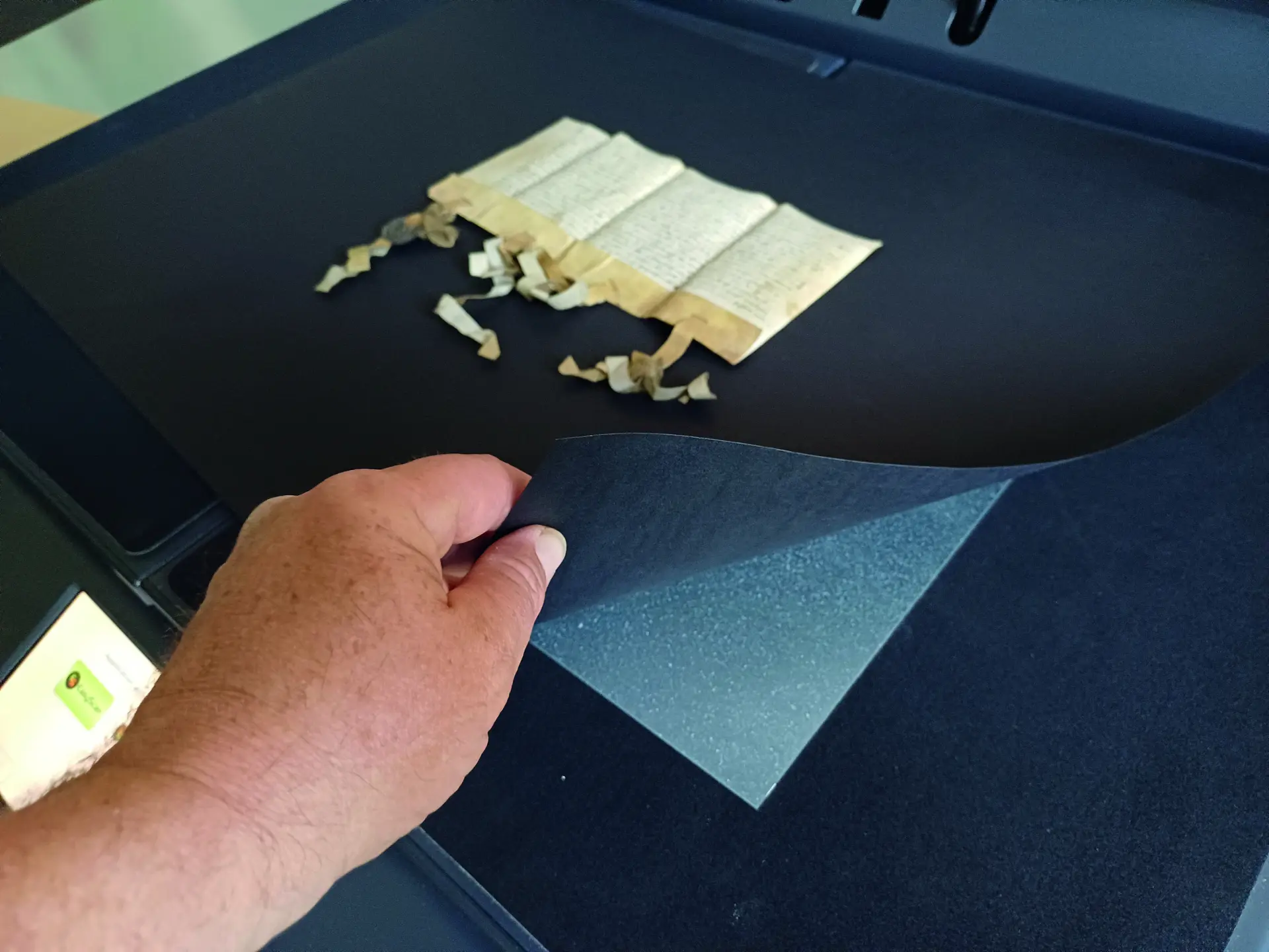 Fixierung einer Urkunde auf nicht magnetischer Aufnahmefläche mithilfe einer schwarzen Pappe und darunter einer magnetischen Platte, um mit Magneten zu fixieren und dann zu digitalisieren 