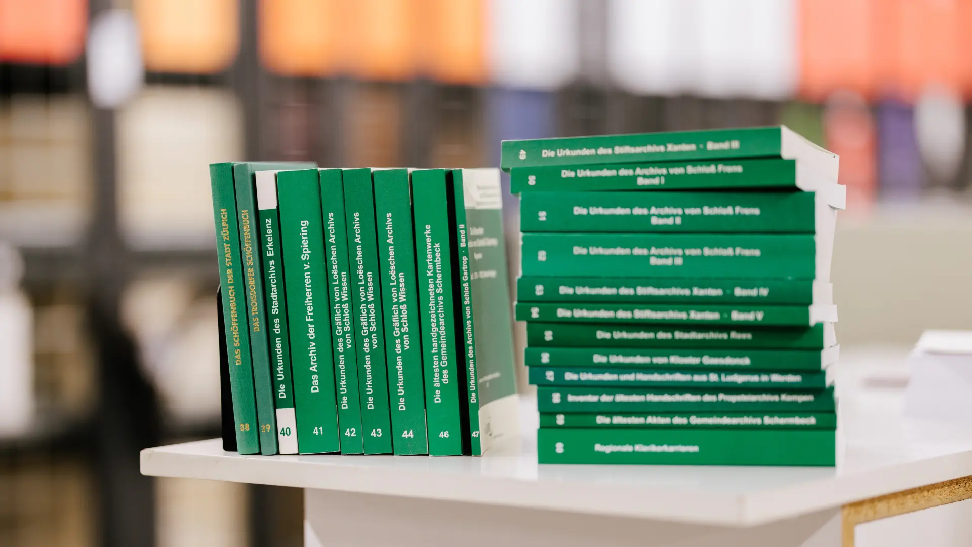 Foto mehrerer grüner Bücher auf einem Tisch, zum Teil als Stapel, zum Teil nebeneinander aufgereiht.
