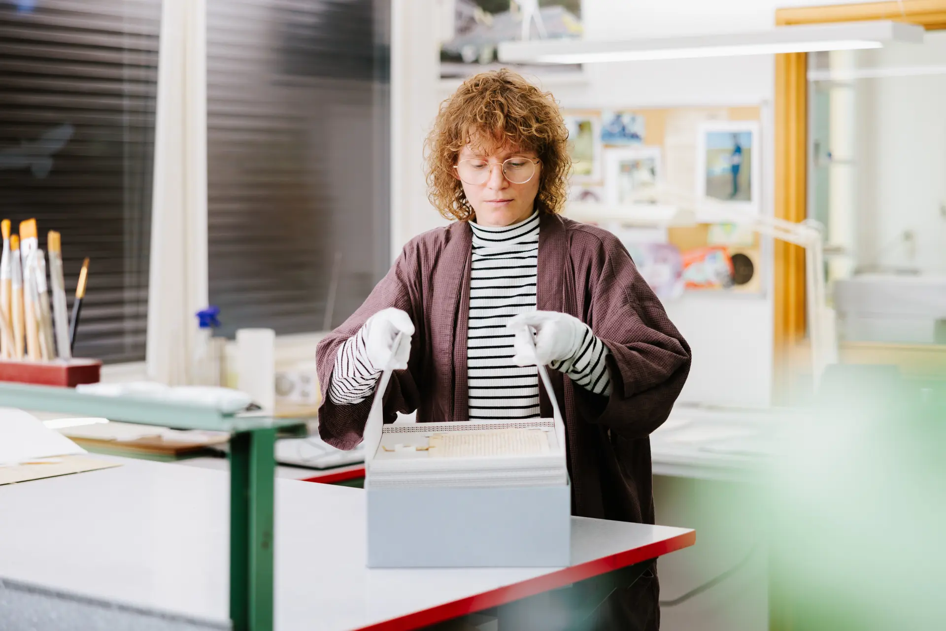 Eine Person entnimmt Objekte mittels einer Aushebehilfe aus dem Archivkarton