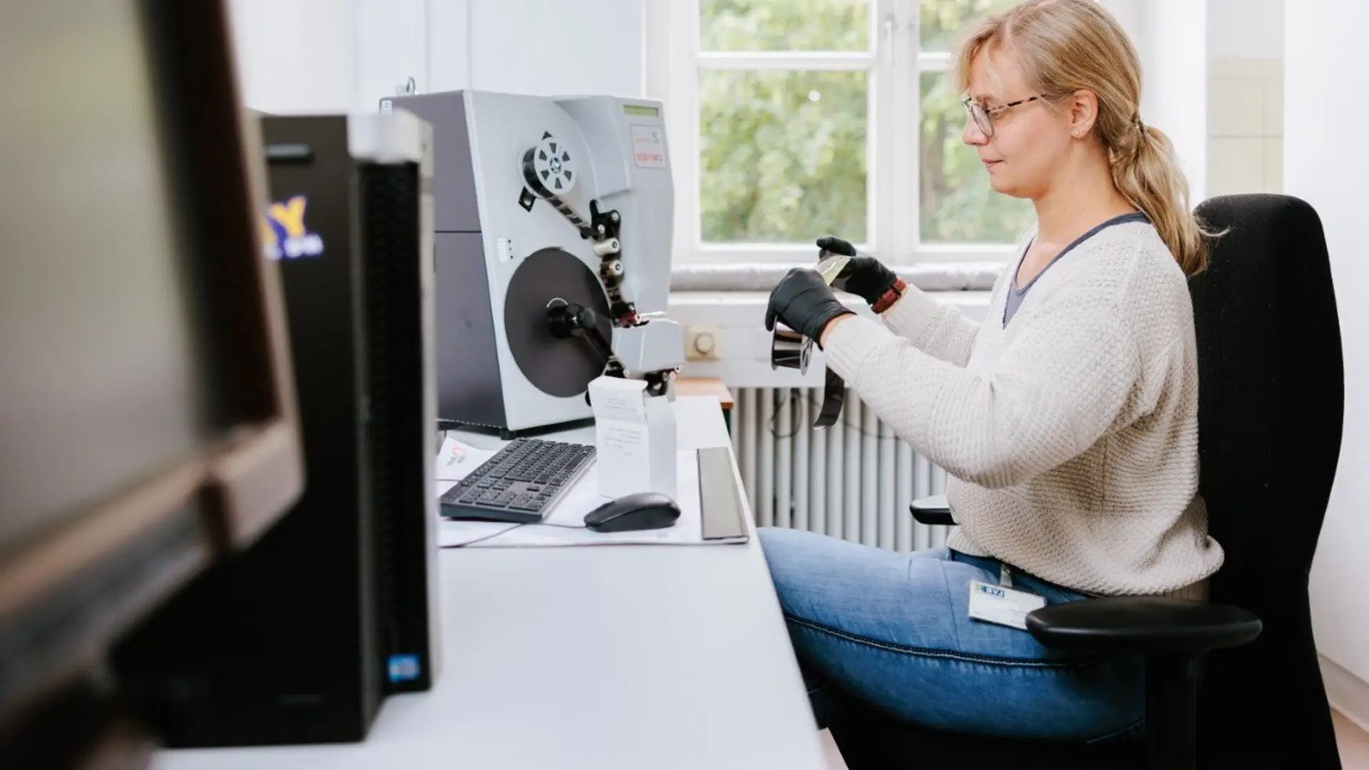 Foto von einer blonden Frau am Computer, die eine Filmrolle hochhält
