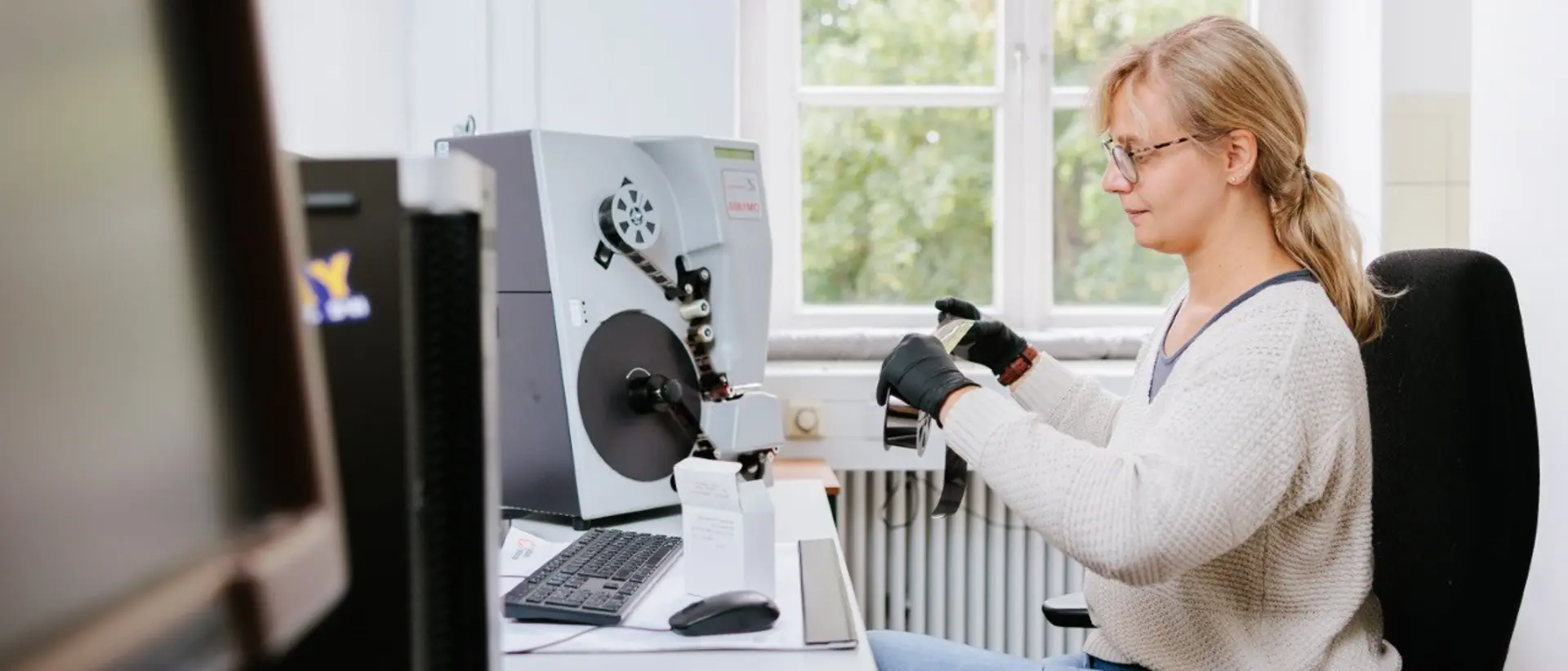 Foto von einer blonden Frau am Computer, die eine Filmrolle hochhält