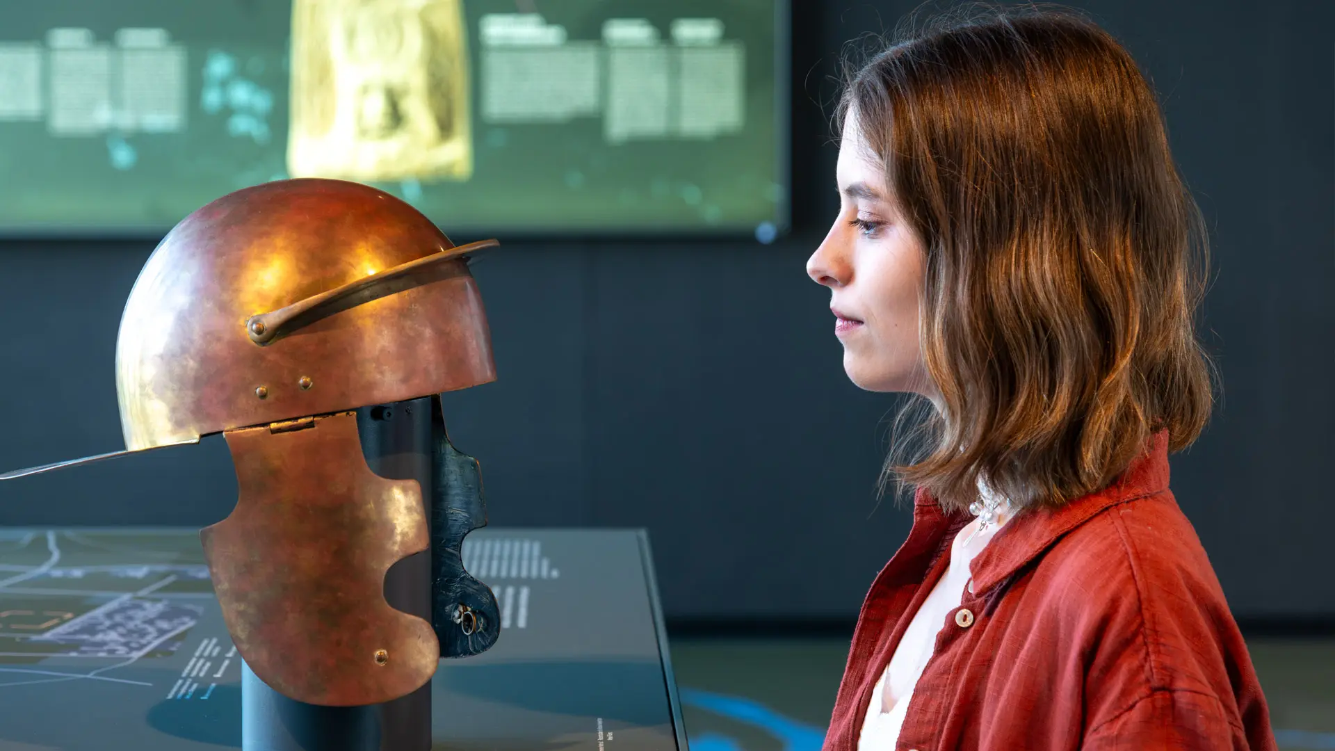 Eine junge Frau steht Auge in Auge mit einem römischen Legionärshelm. Sie und der Helm sind im Profil sichtbar.