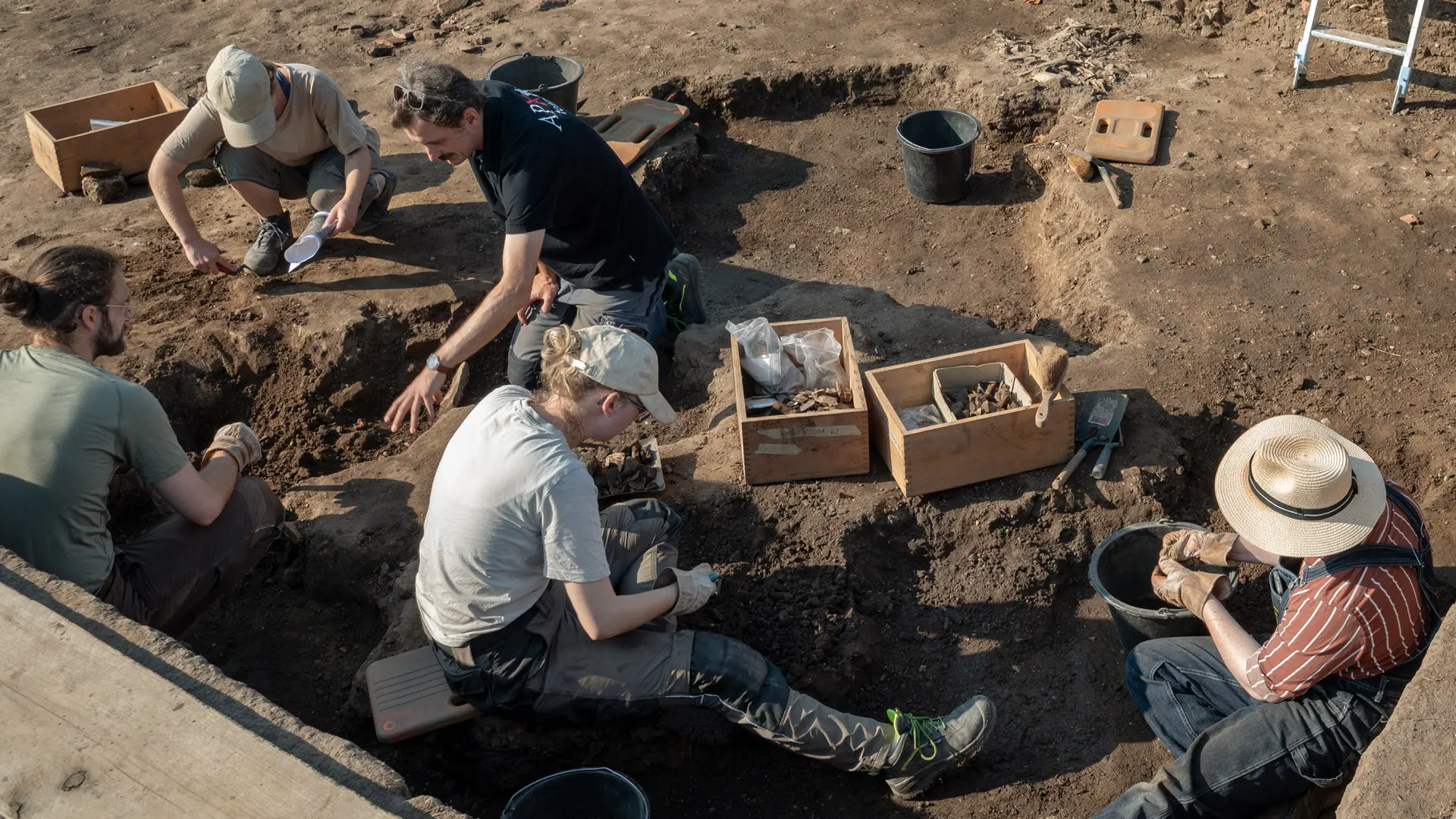 Grabung Live, Archäologin erläutert Kindern die Grube unter einem Sonnenpavillon