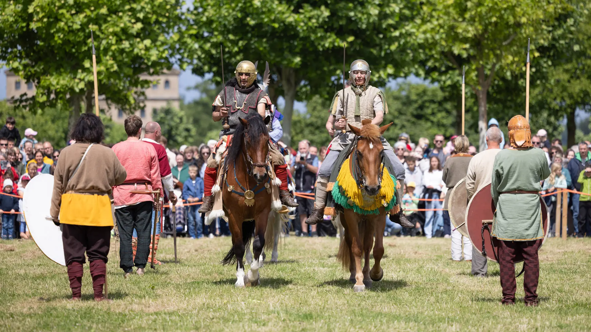 Zwei Reiter reiten durch ein Spalier von Germanen, im Hintergrund Publikum