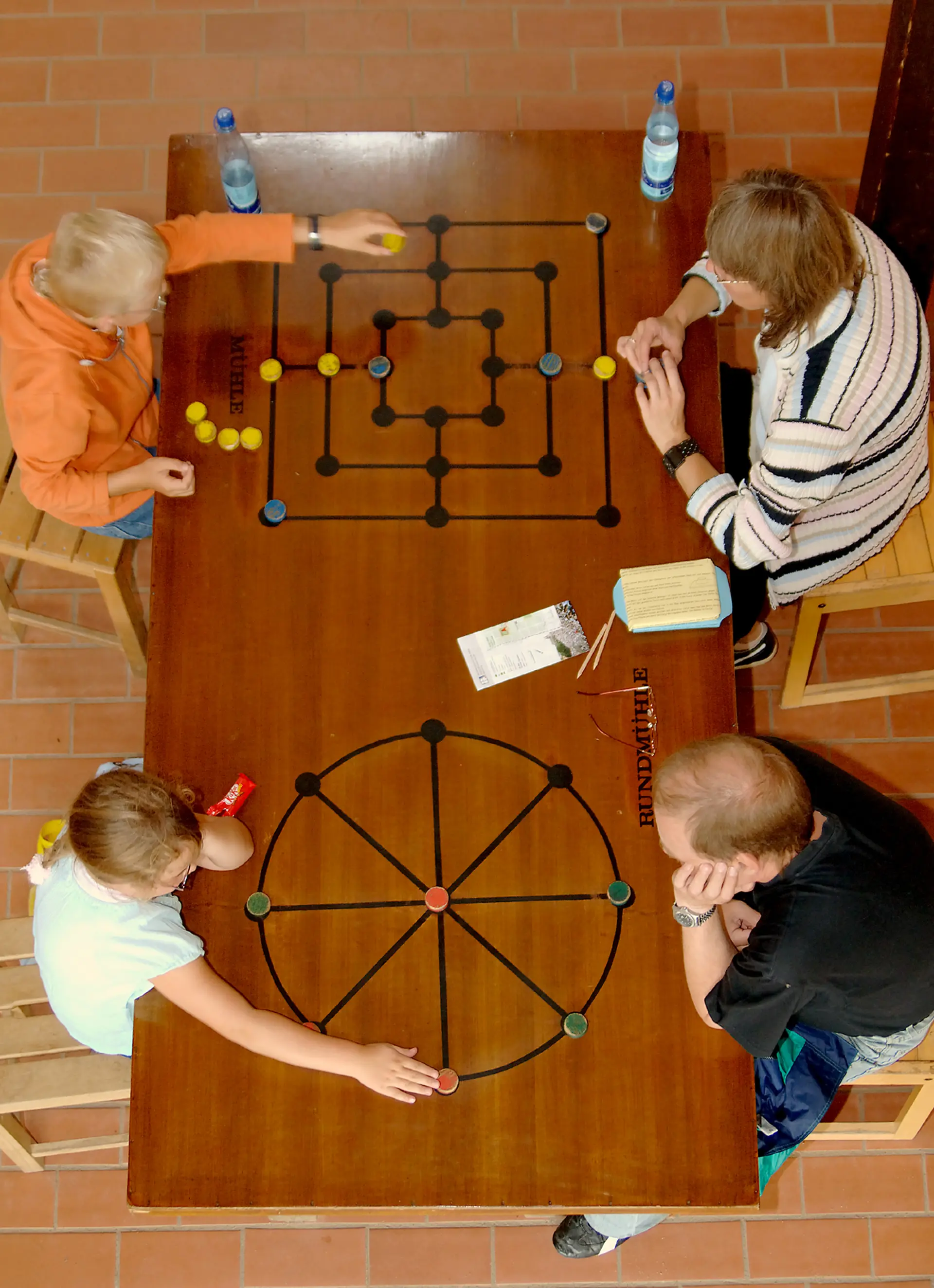 Spielehaus, Blick von oben auf einen Spieltisch mit Spielbrettern und vier Kindern drumherum 
