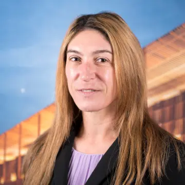 Ein Portraitfoto einer Frau mit rotblonden langen Haaren, einem lila Oberteil und schwarzen Blazer, die lächelnd in die Kamera schaut.