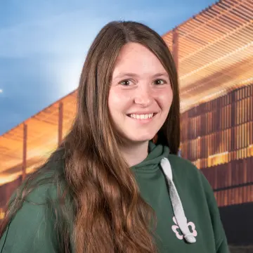 Portraitfoto einer Frau mit grünem Pullover und dunklen, langen Haaren, die lächelnd in die Kamera schaut.