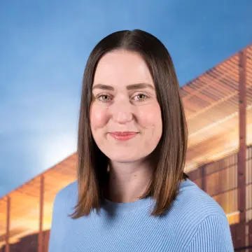Portraitfoto einer Frau mit dunklem Haar und einem hellblauen Pullover, die lächelnd in die Kamera schaut.