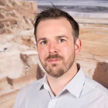 Portraitfoto eines Mannes mit einem weißen Hemd und kurzem Bart.