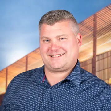 Portraitfoto eines Mannes mit blauem Hemd und kurzen grauen Haaren, der lächelnd in die Kamera schaut.