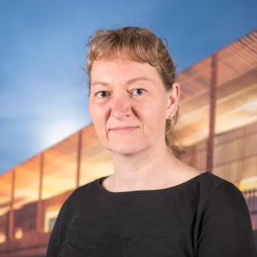 Portraitfoto einer Frau mit blondem Zopf und einem schwarzen Oberteil, die in die Kamera lächelt.