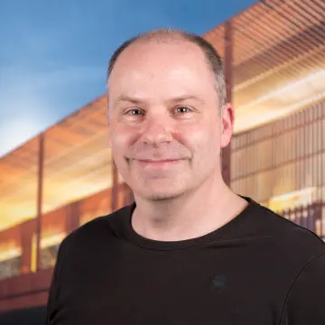 Portraitfoto eines Mannes mit Halbglatze und einem schwarzen Oberteil, der in die Kamera lächelt.