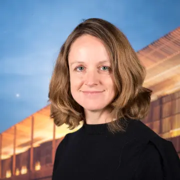Portraitfoto einer Frau mit schulterlangem Haar und einem schwarzen Pullover, die lächelnd in die Kamera schaut.