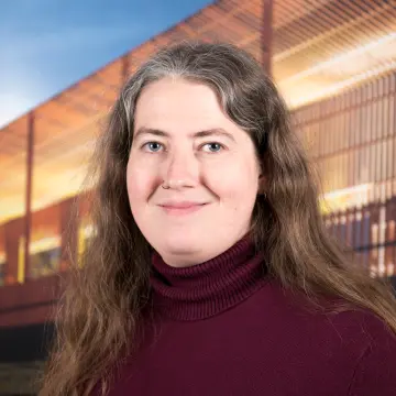 Portraitfoto einer Frau mit rotem Pullover und langen, dunklen Locken, die in die Kamera lächelt.