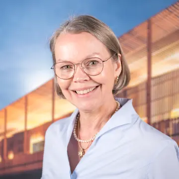 Portraitfoto einer Frau mit einer Brille, kinnlangem Haar und einer hellblauen Bluse, die lächelnd in die Kamera schaut.