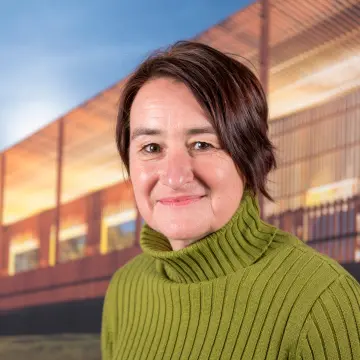 Portraitfoto einer Frau mit kurzen, rotbraunem Haar und einem grünen Pullover, die lächelnd in die Kamera schaut.