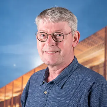 Portraitfoto eines Mannes mit Brille und einem blauen Hemd, lächelt in die Kamera.