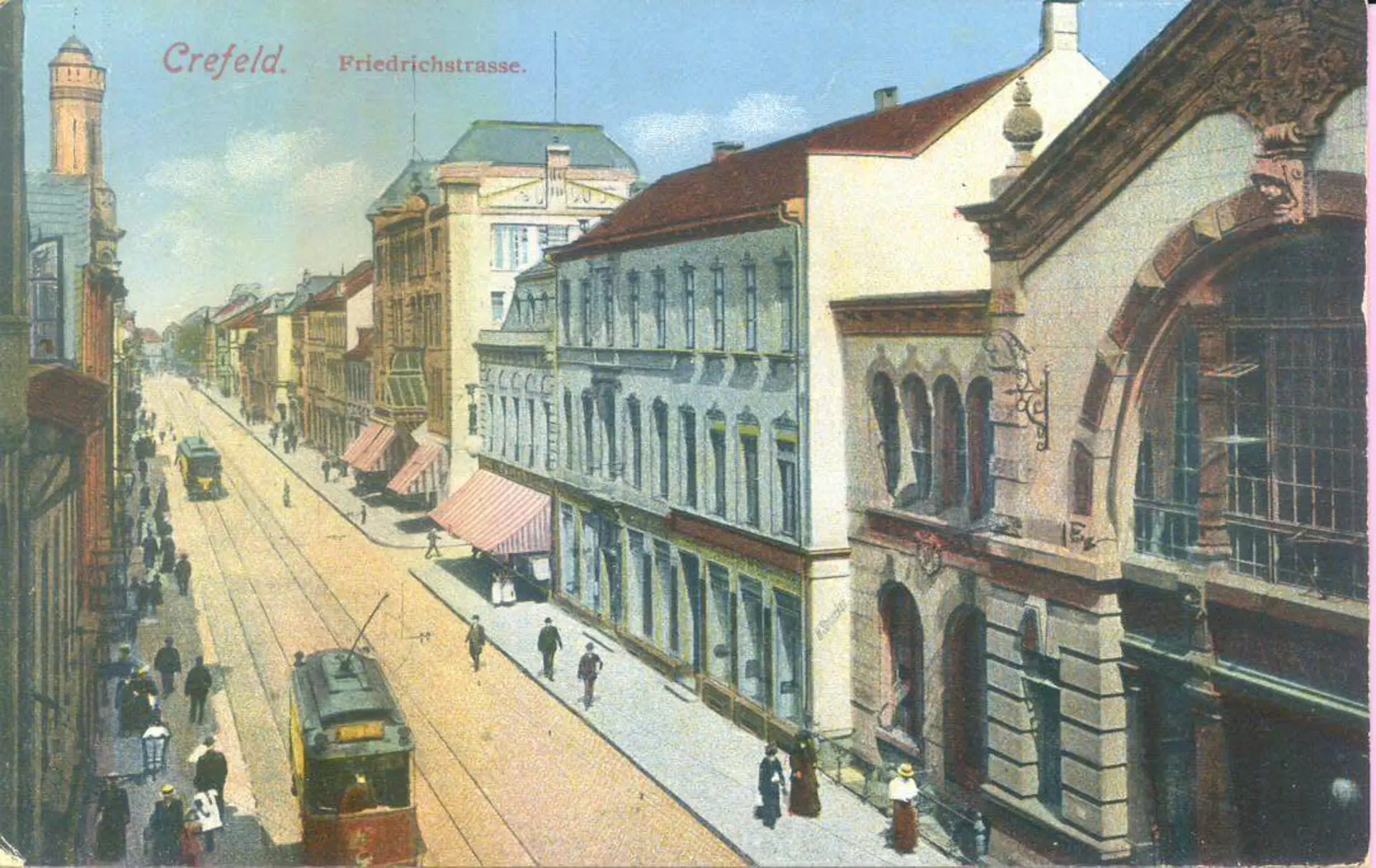 Historische, kolorierte Ansicht der Friedrichstraße in Crefeld (heute Krefeld). Die breite Straße mit Straßenbahngleisen wird von mehrstöckigen Geschäfts- und Wohnhäusern gesäumt. Eine Straßenbahn fährt im Vordergrund, eine weitere ist in der Ferne zu sehen. Fußgänger bewegen sich auf den Gehwegen.