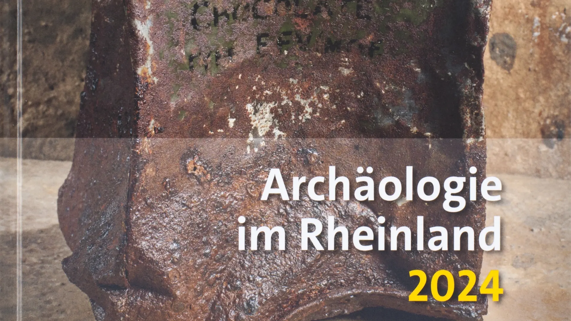 Coverfoto der Archäologie im Rheinland 2024. Das Bild zeigt eine rostige Metallbox mit Aufschrift.
