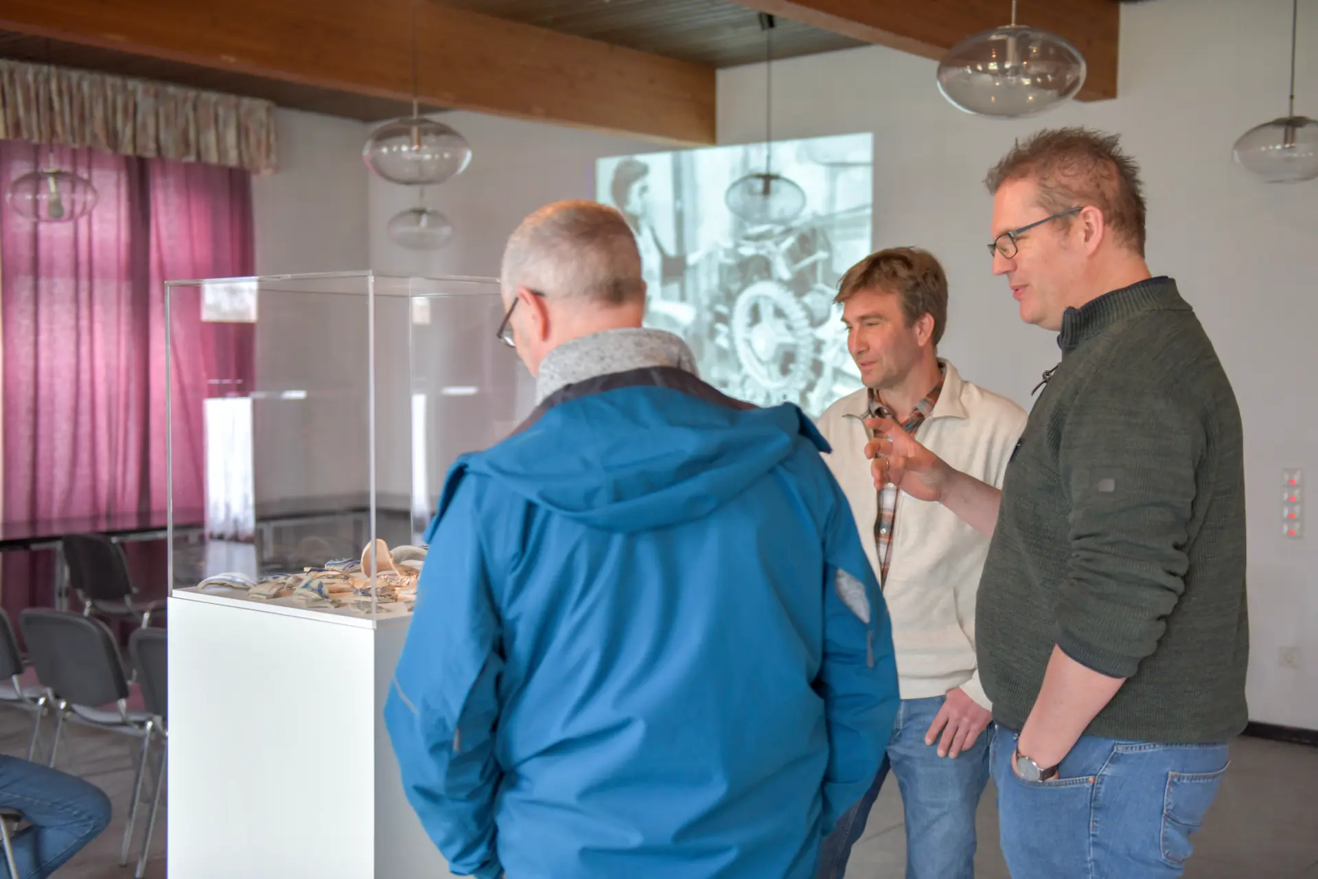 Drei Männer stehen um eine Glasvitrine, in der Keramikscherben ausgelegt sind.