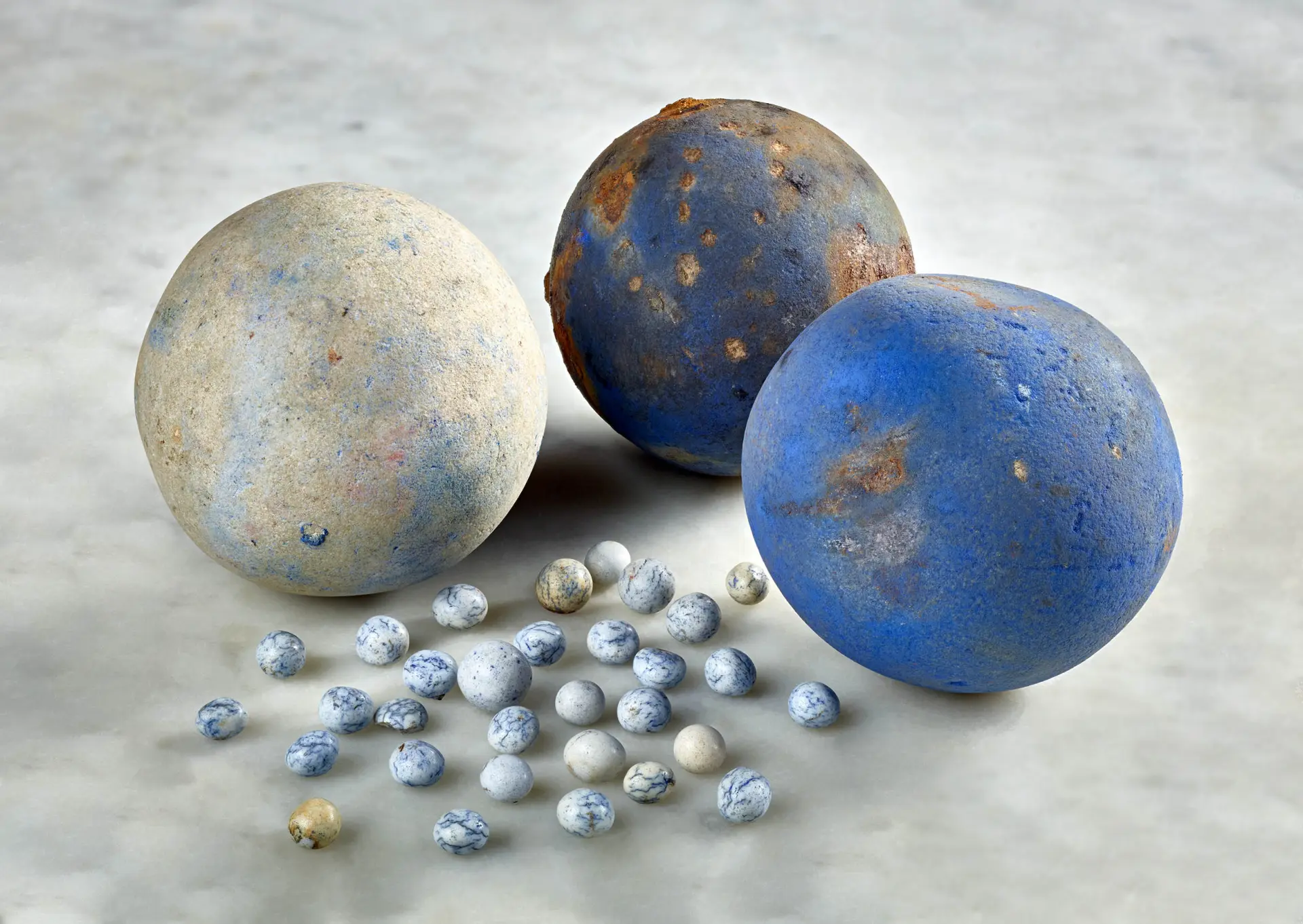 Drei große Kugeln mit kräftiger blauer Farbe und mehrere kleine weiß-blaue Kügelchen liegen auf einer weißen Marmorplatte.