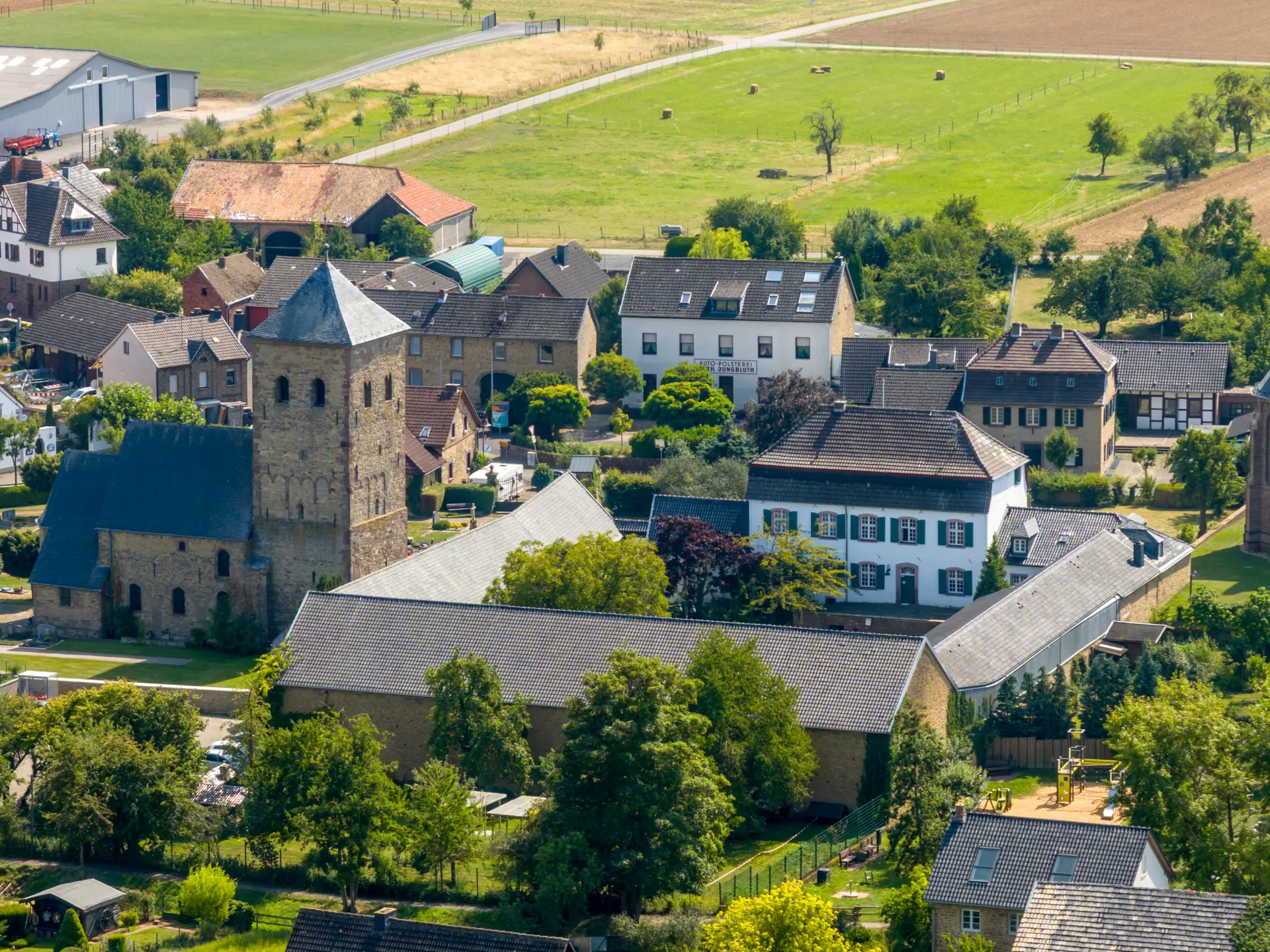 Das Foto wurde aus der Luft gemacht. Links im Bild ist eine Kirche und rechts daneben eine Hofanlage. Umgeben ist das Gelände von Wohnhäusern und Gärten.