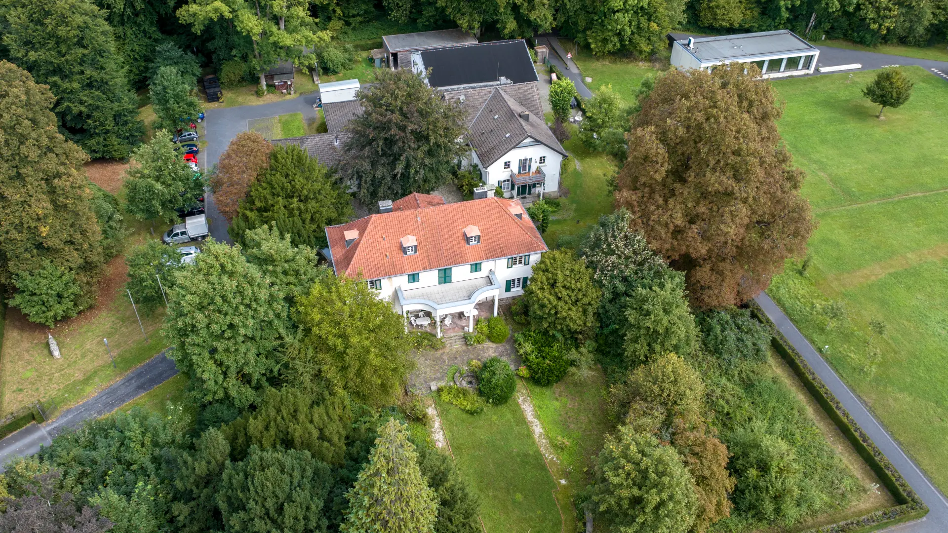 Ein Gutshof bestehend aus verschiedenen Gebäude aus der Luft fotografiert. Um den Gutshof sind Wiesen und Waldflächen.