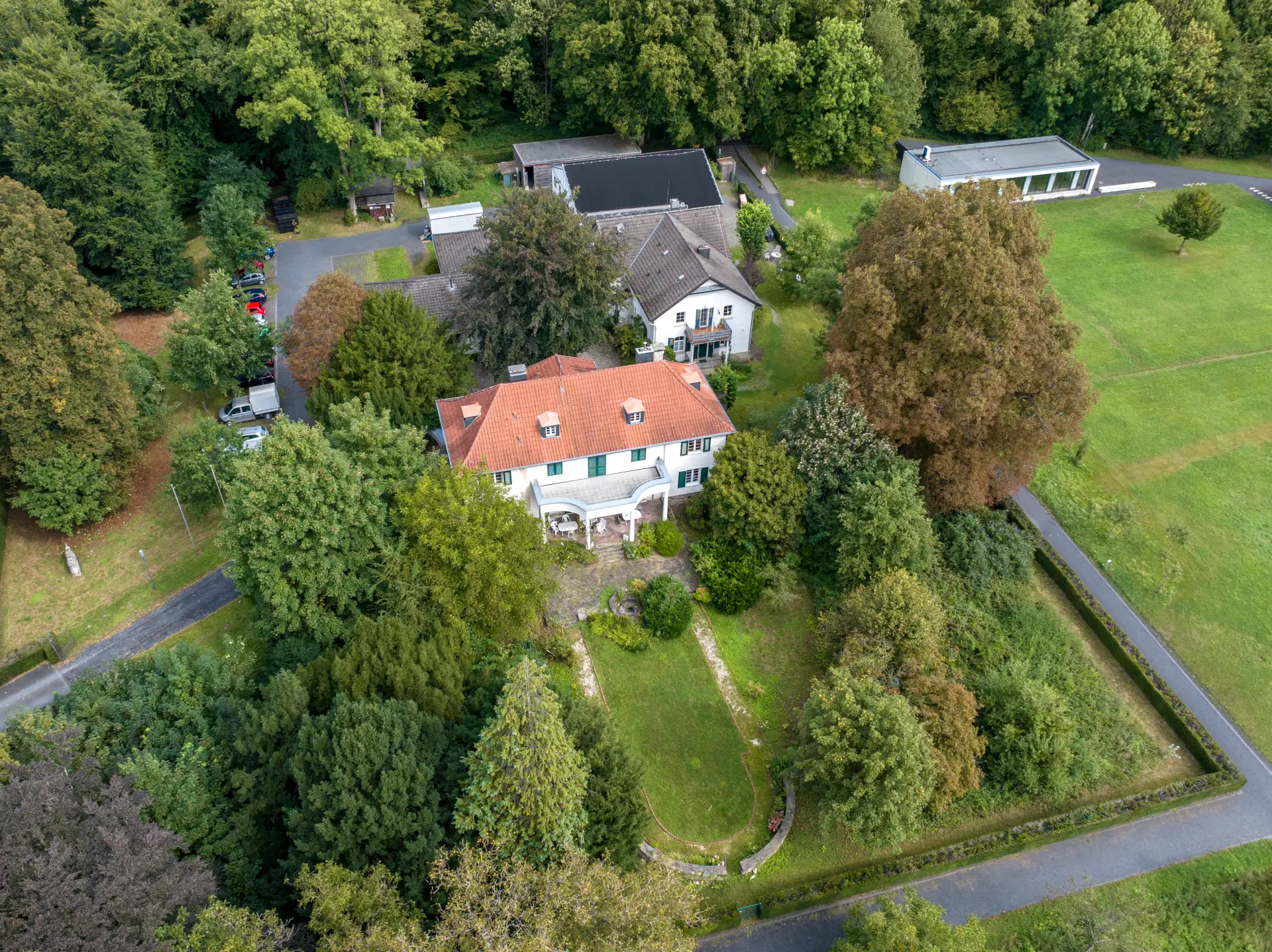 Ein Gutshof bestehend aus verschiedenen Gebäude aus der Luft fotografiert. Um den Gutshof sind Wiesen und Waldflächen.