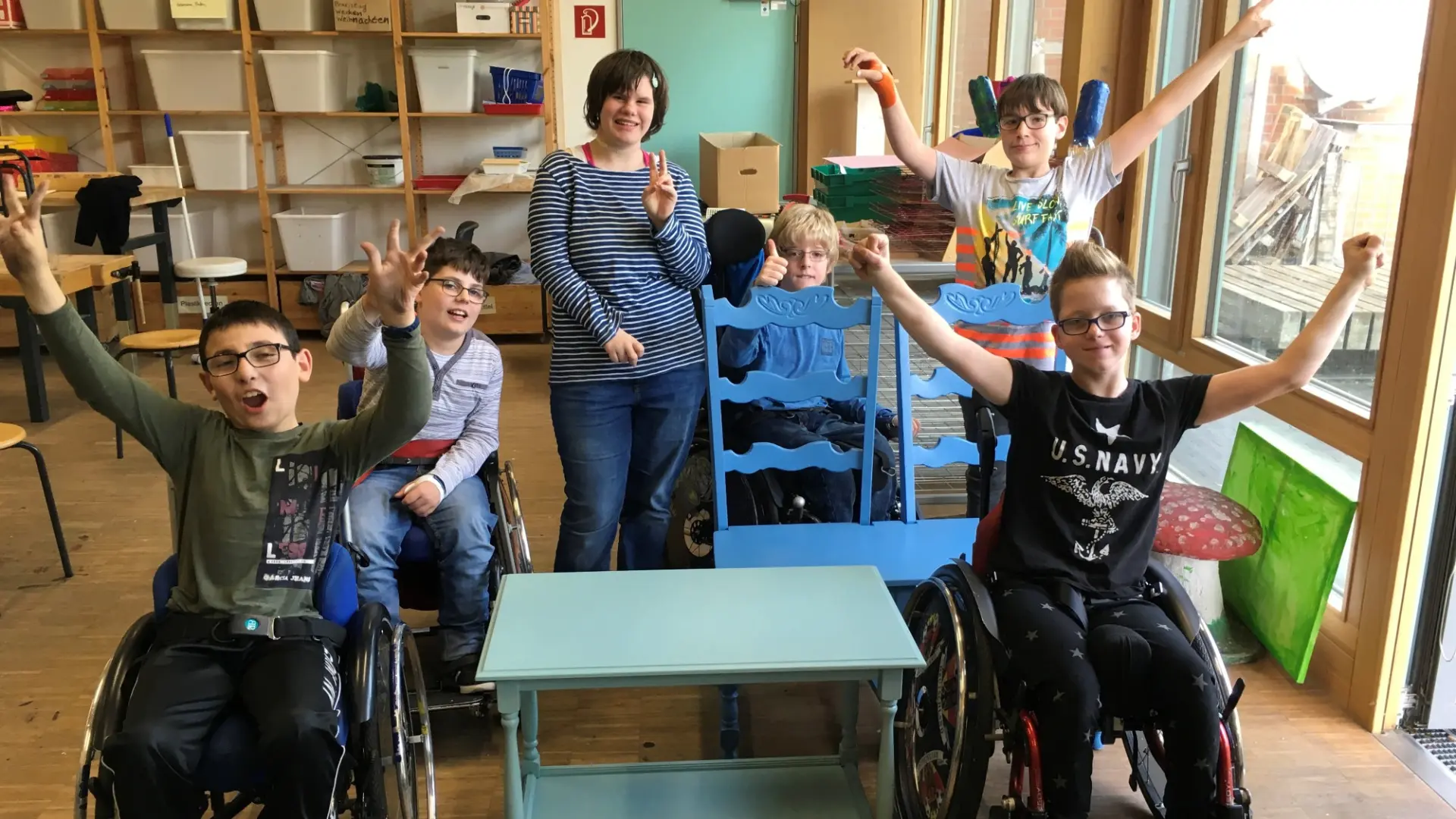 In einem Klassenraum: Fünf Kinder - zum Teil im Rollstuhl - recken glücklich die Arme in die Höhe, weil sie etwas gewonnen haben.