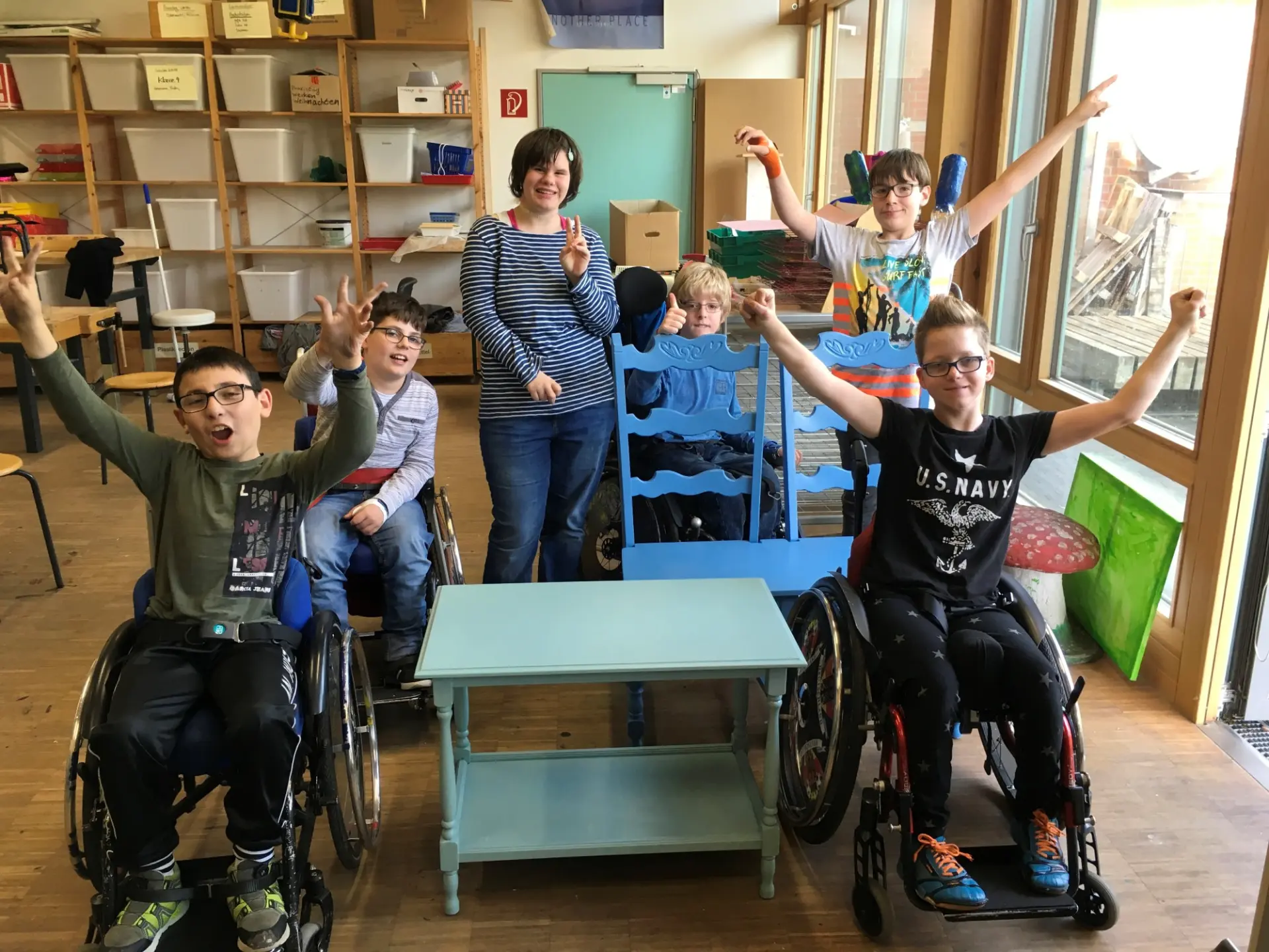 In einem Klassenraum: Fünf Kinder - zum Teil im Rollstuhl - recken glücklich die Arme in die Höhe, weil sie etwas gewonnen haben.
