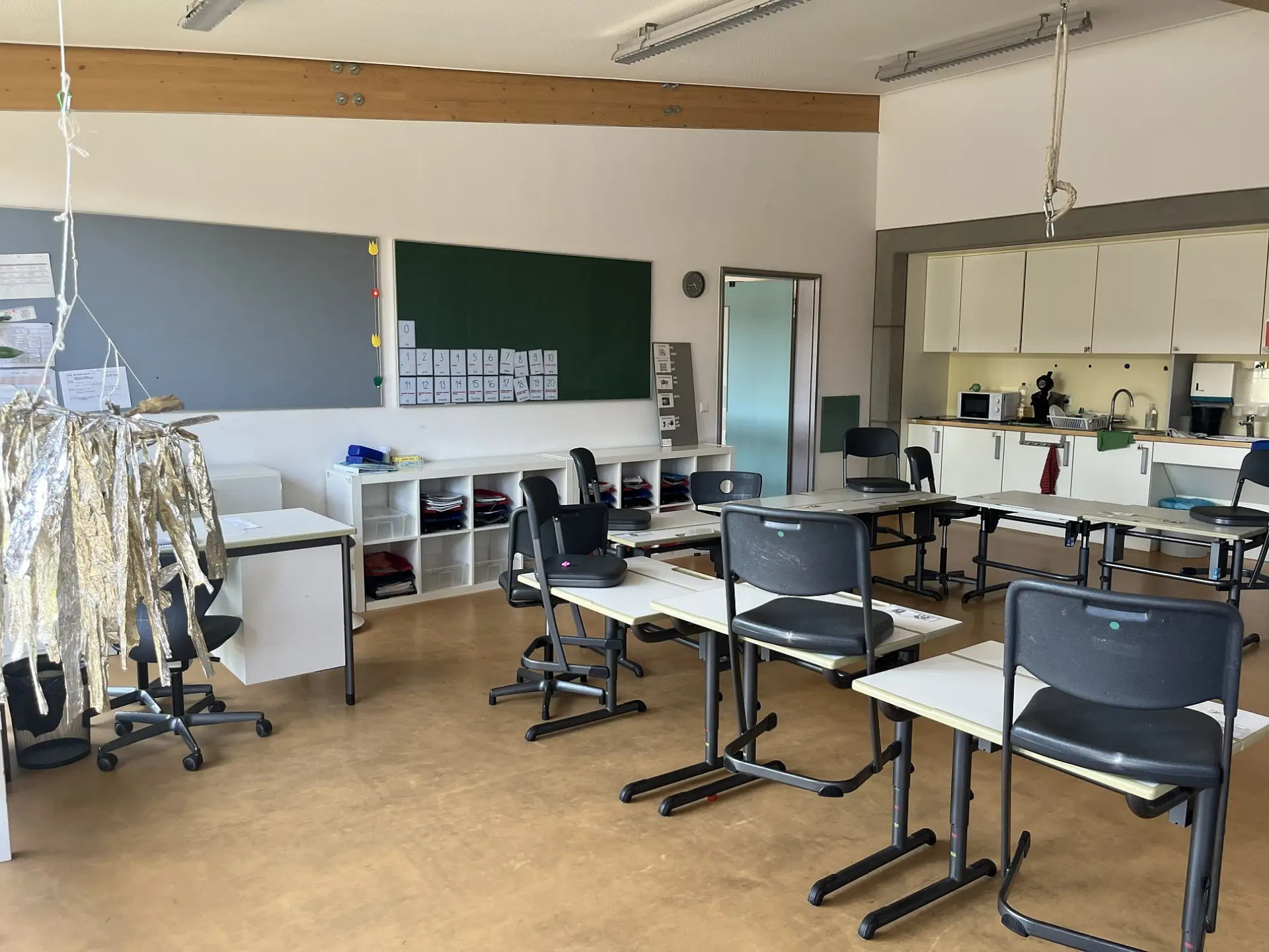 Klassenraum mit Einbauküche, Einzeltischen und Schultafeln