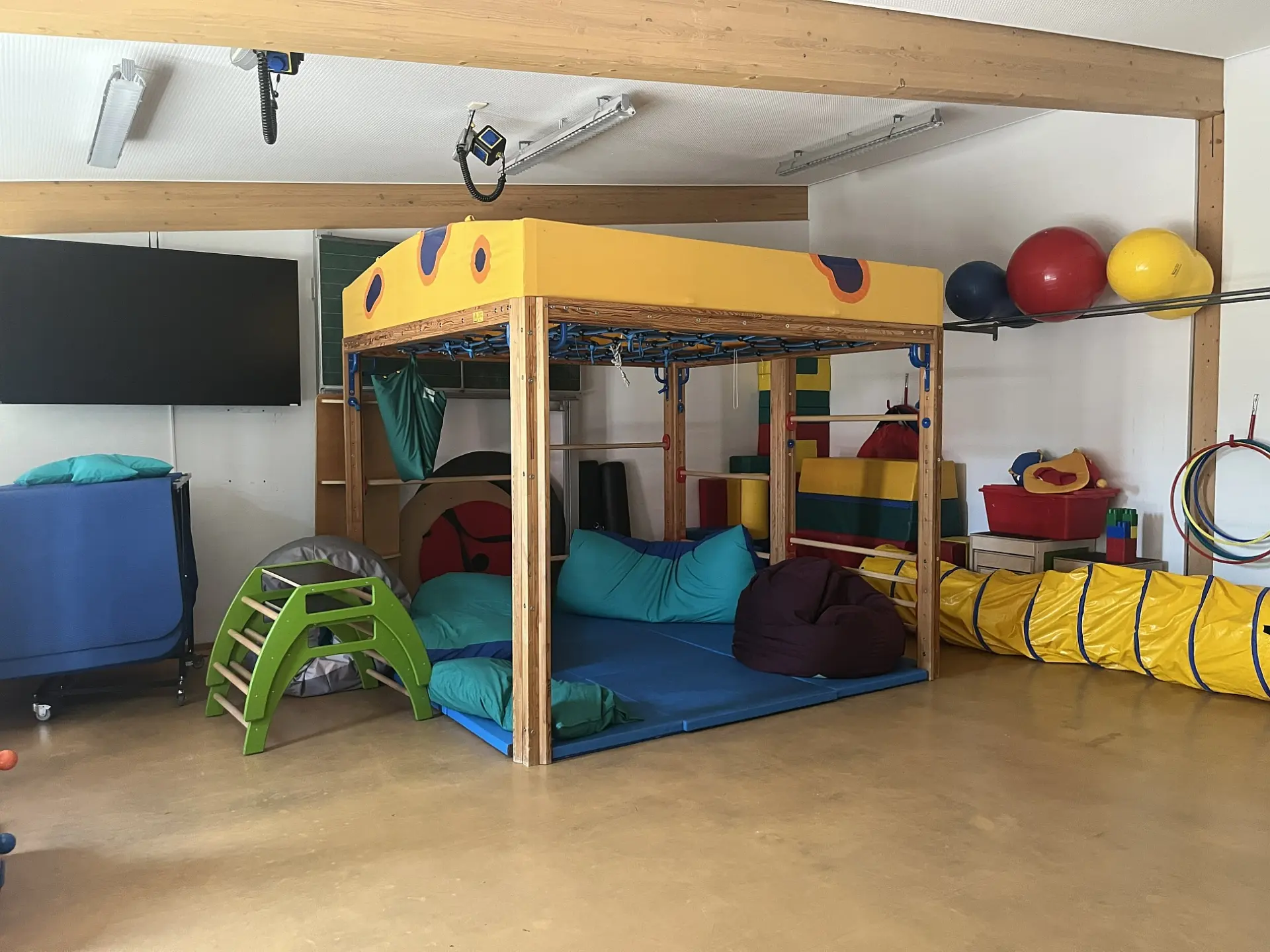 heller Raum mit Klettergerüst, bunten Polstern, Bällen und Kriechtunnel