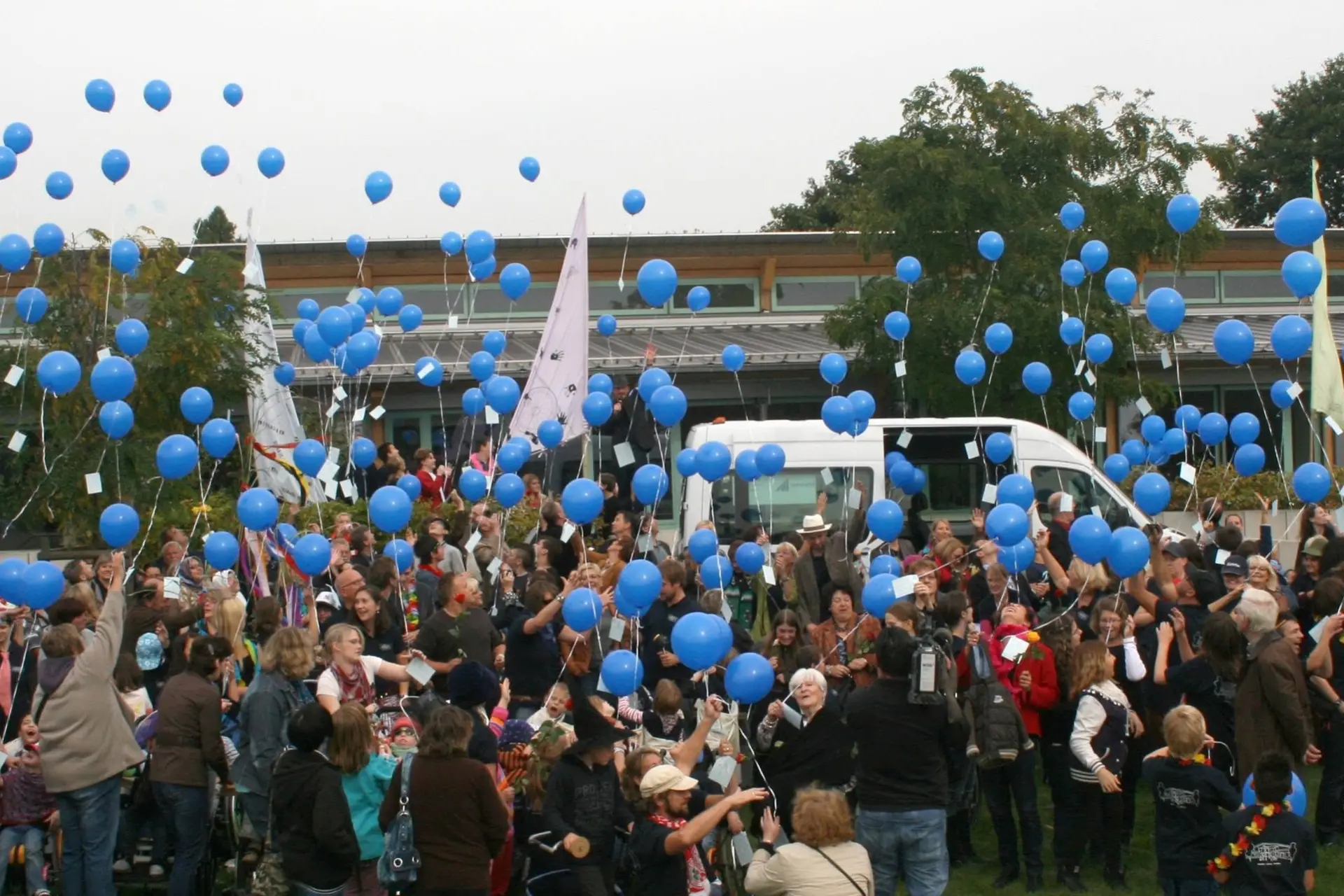 Eine große Gruppe Menschen vor mit heliumgefüllten Luftballons, die sie an Bändern in die Luft halten.