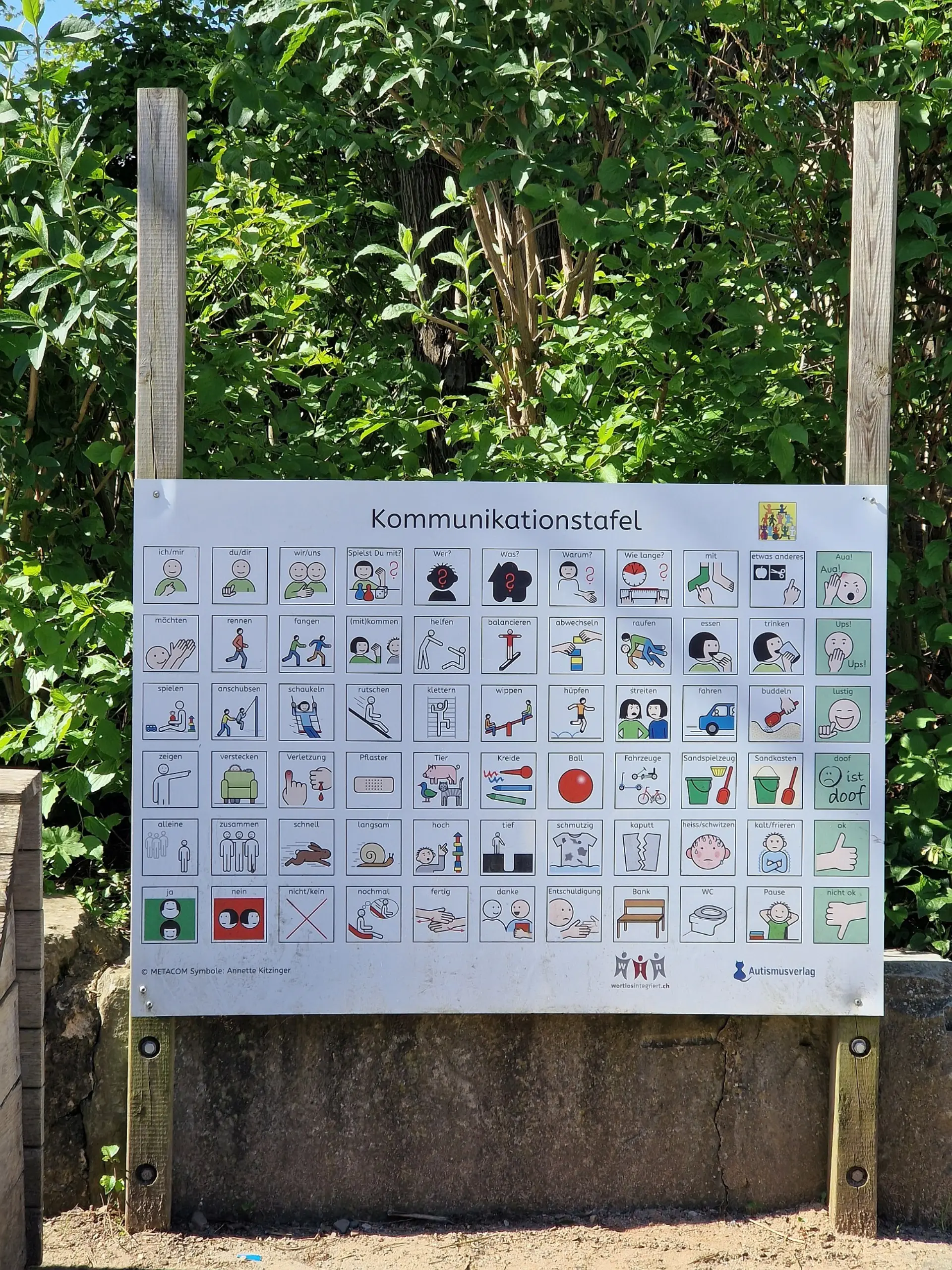 Eine große Kommunikationstafel mit mehreren Zeilen und Spalten mit verschiedenen Metacom-Symbole im grünen Schulinnenhof