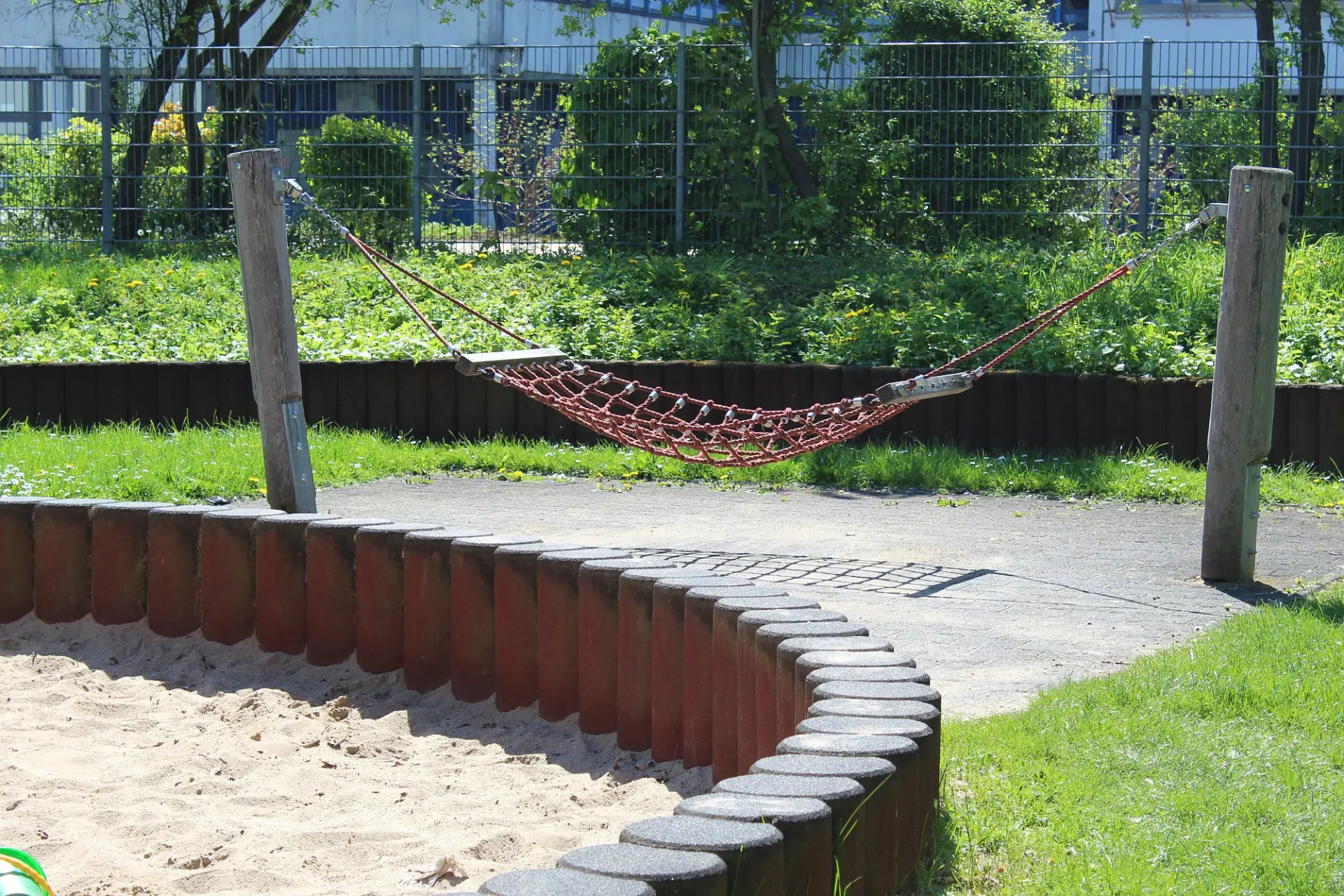 Ein Teil des Spielplatzes im Innenhof: Links ist ein großer Sandkasten, rechts eine Netz-Hängematte zu sehen.