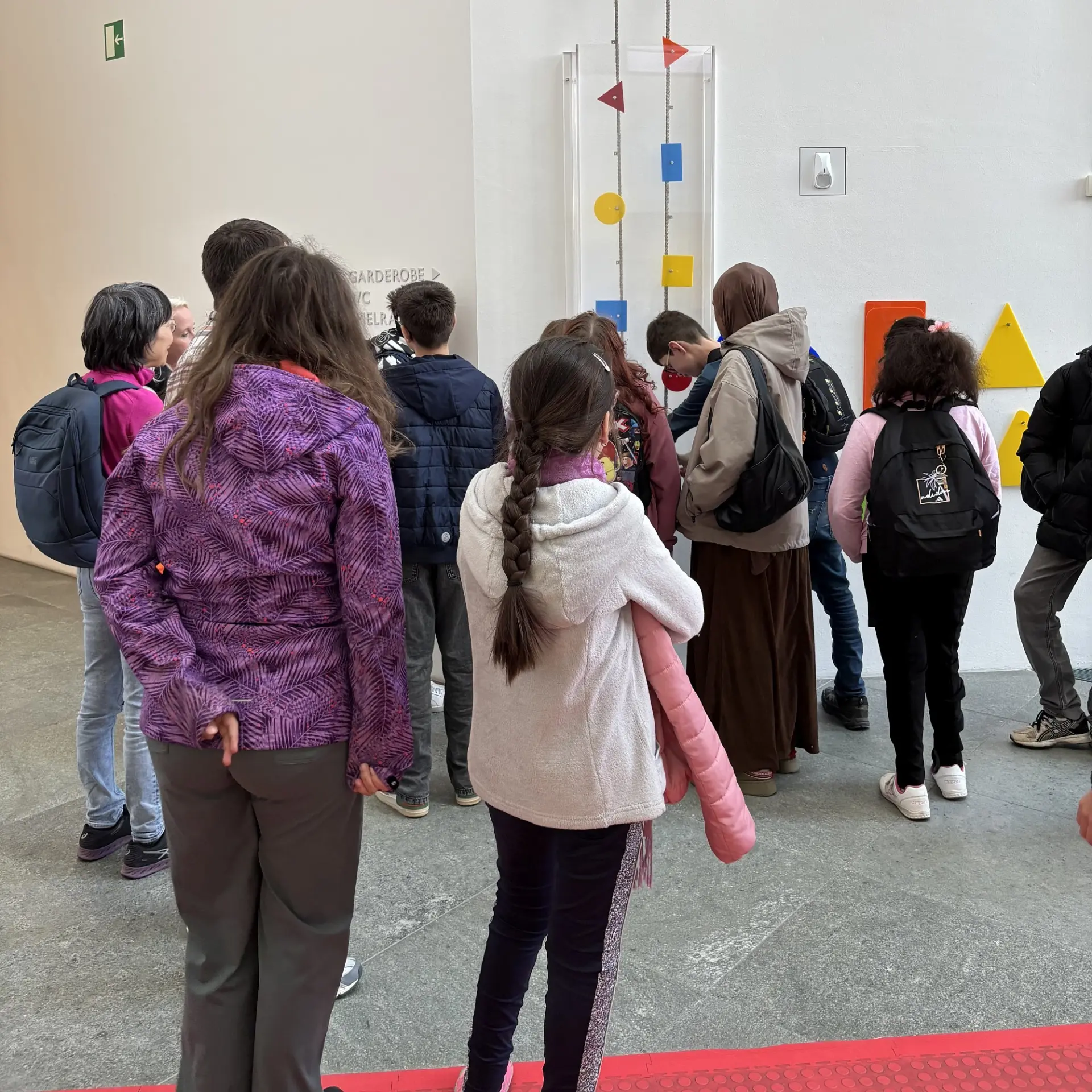 Eine Gruppe von Jugendlichen steht in einem Museum und schaut sich eine Wandinstallation an.