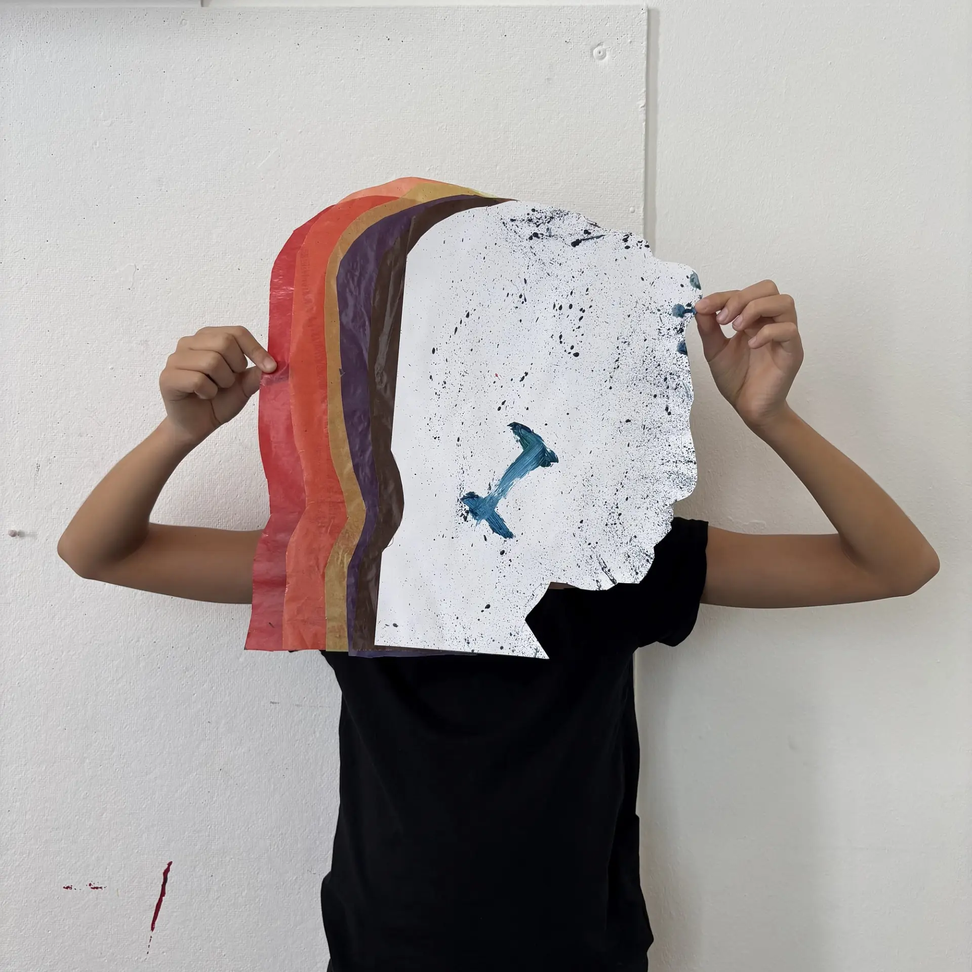 Ein Schulkind hält mit beiden Händen ein mehrschichtiges Kunstwerk aus Papier vor sein Gesicht. Das Kunstwerk zeigt die Silhouette eines Kopfes im Profil.