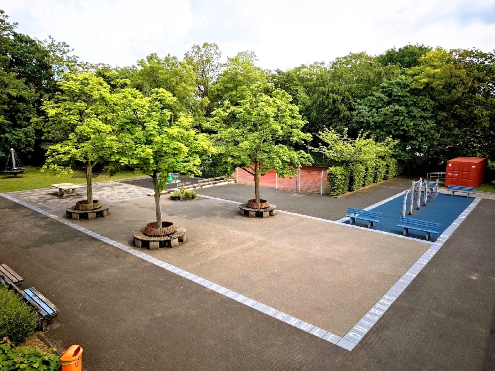 Pausenhof der Schule mit Bänken und Bäumen