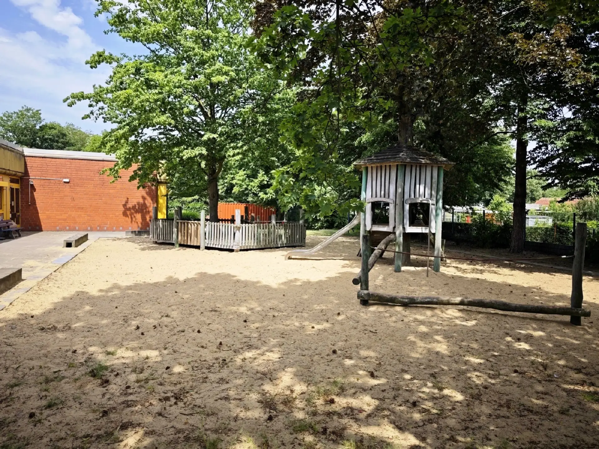 Pausenhof mit großem Sandkasten und Baumhaus