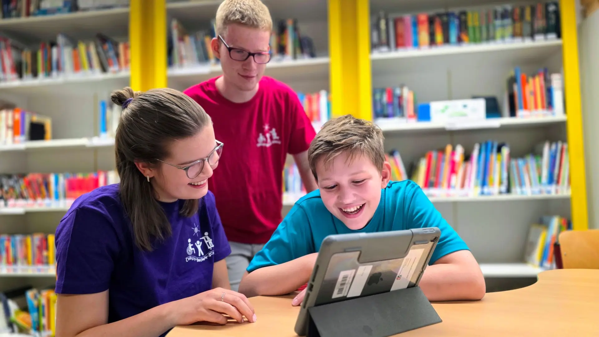 Drei Jugendliche arbeiten in Bibliothek mit Tablet