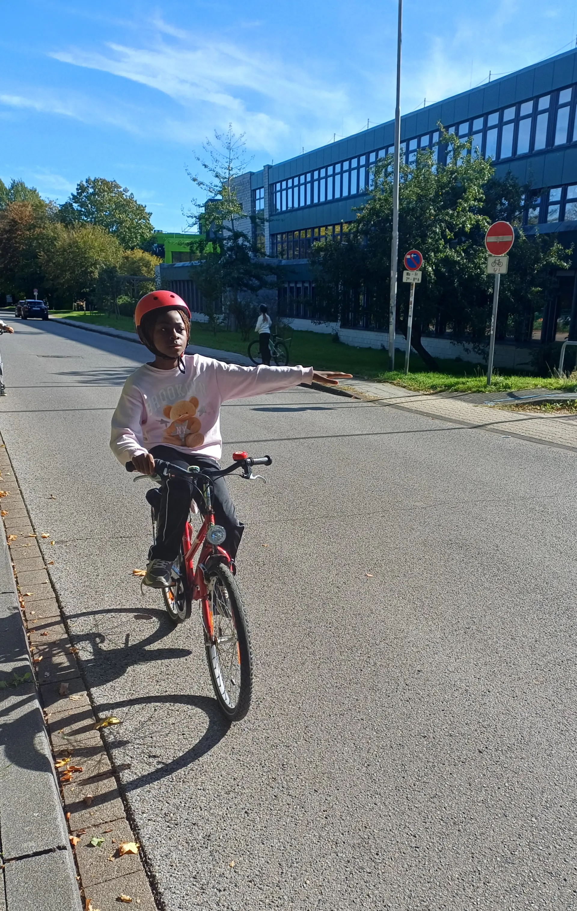 Auf dem Bild ist eine Schülerin der Klasse 4 zu sehen, die auf ihrem Fahrrad sitzt und ein Handzeichen zum Abbiegen gibt.